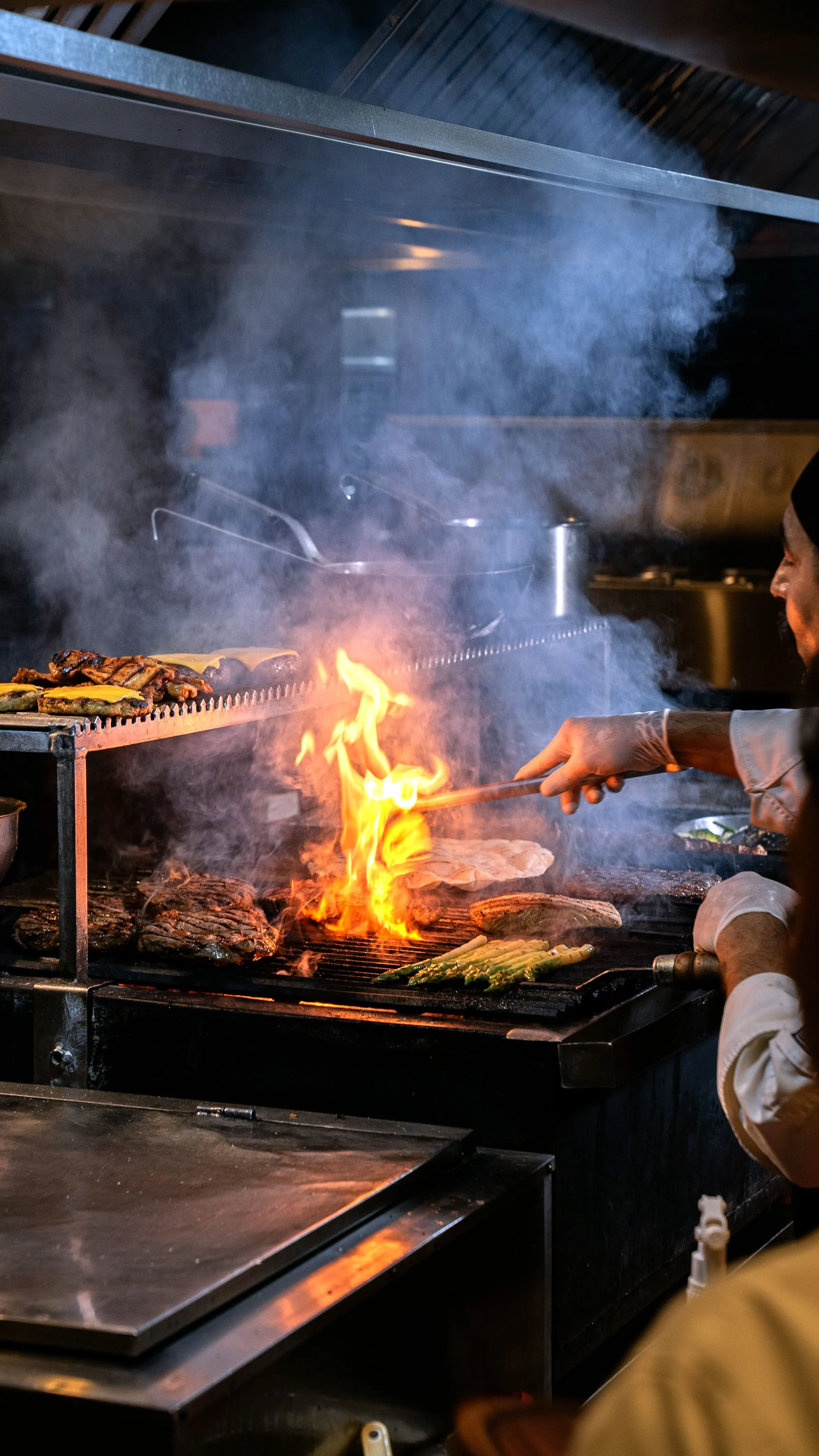 Parrillero avivando el fuego de la brasa en la cocina abierta de Artebe, entre humo y llama