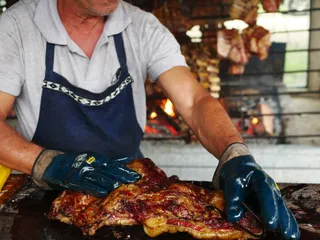 Manos enguantadas sacando una pieza de carne asada de la brasa
